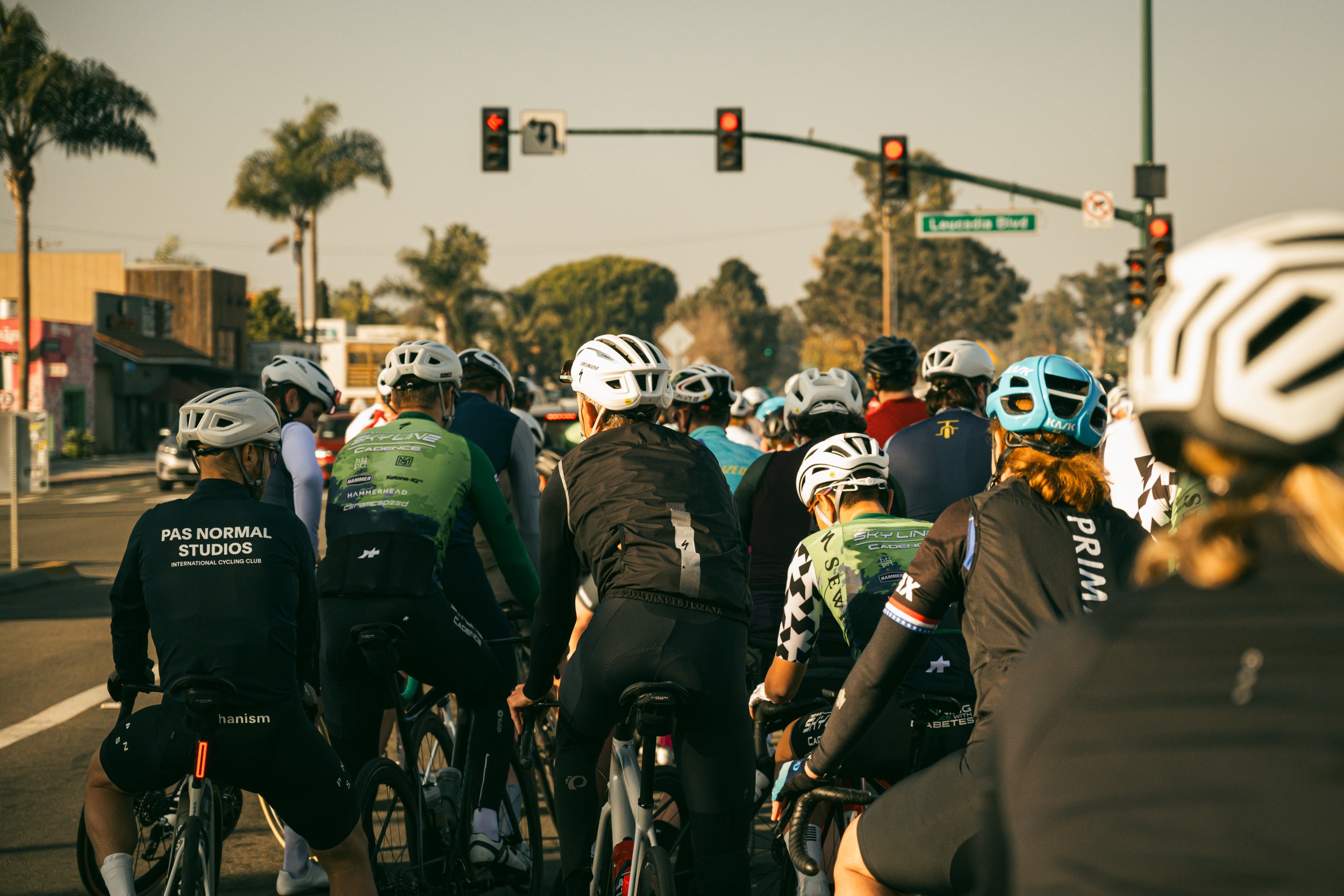 Group of cyclists waiting at a traffic light with palm trees in the background in Encinitas California.