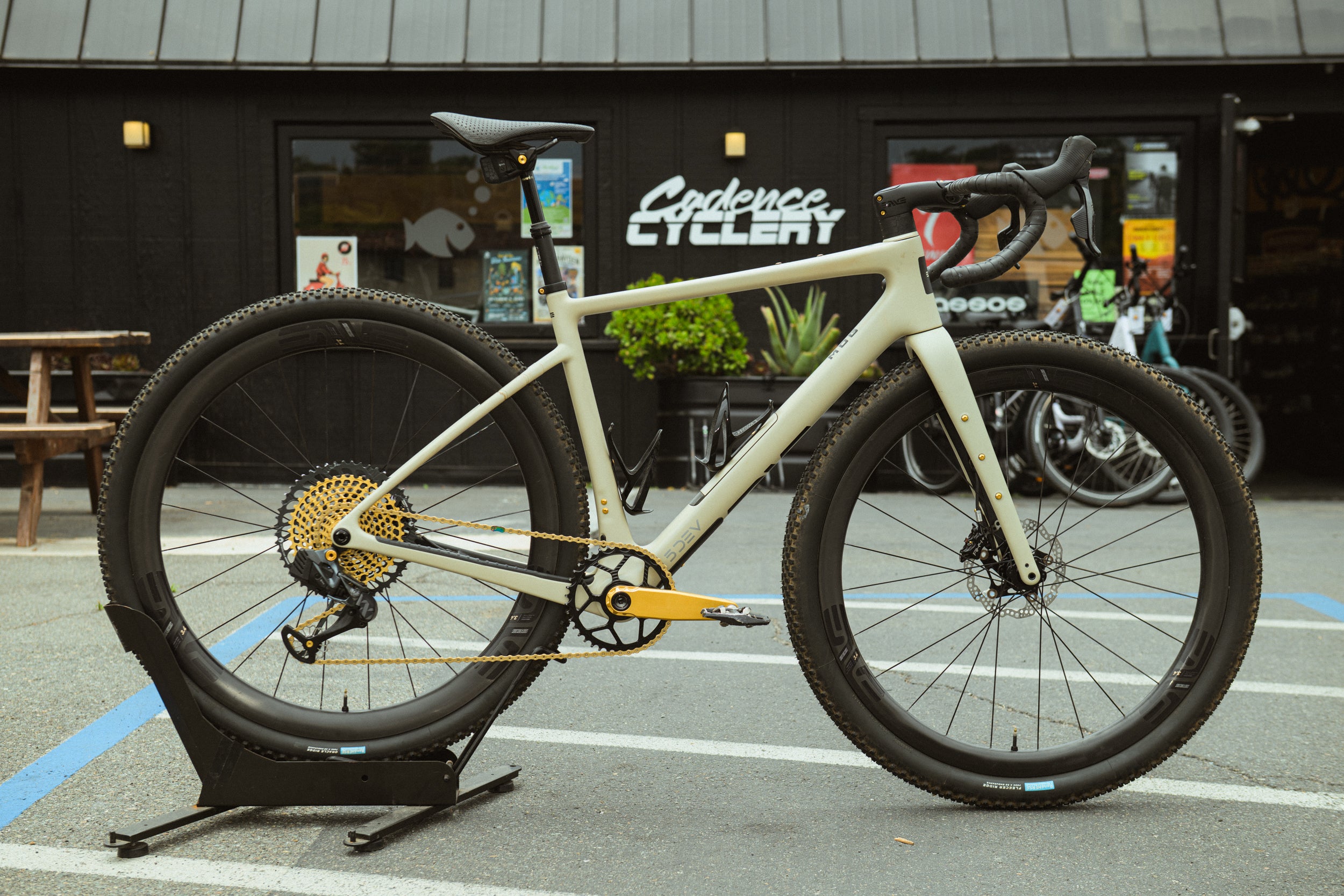 Enve MOG custom gravel bike on a stand in front of a building with Cadence Cyclery branding.
